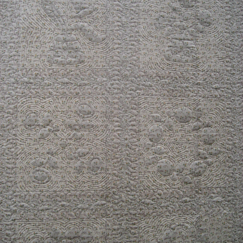 A close-up of a light gray quilted fabric with a repeating floral and scroll pattern.