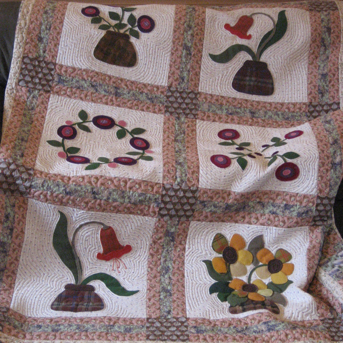 A handmade quilted patchwork blanket featuring six floral and botanical panels with appliques of flowers, leaves, and berries, bordered by a floral patterned fabric.