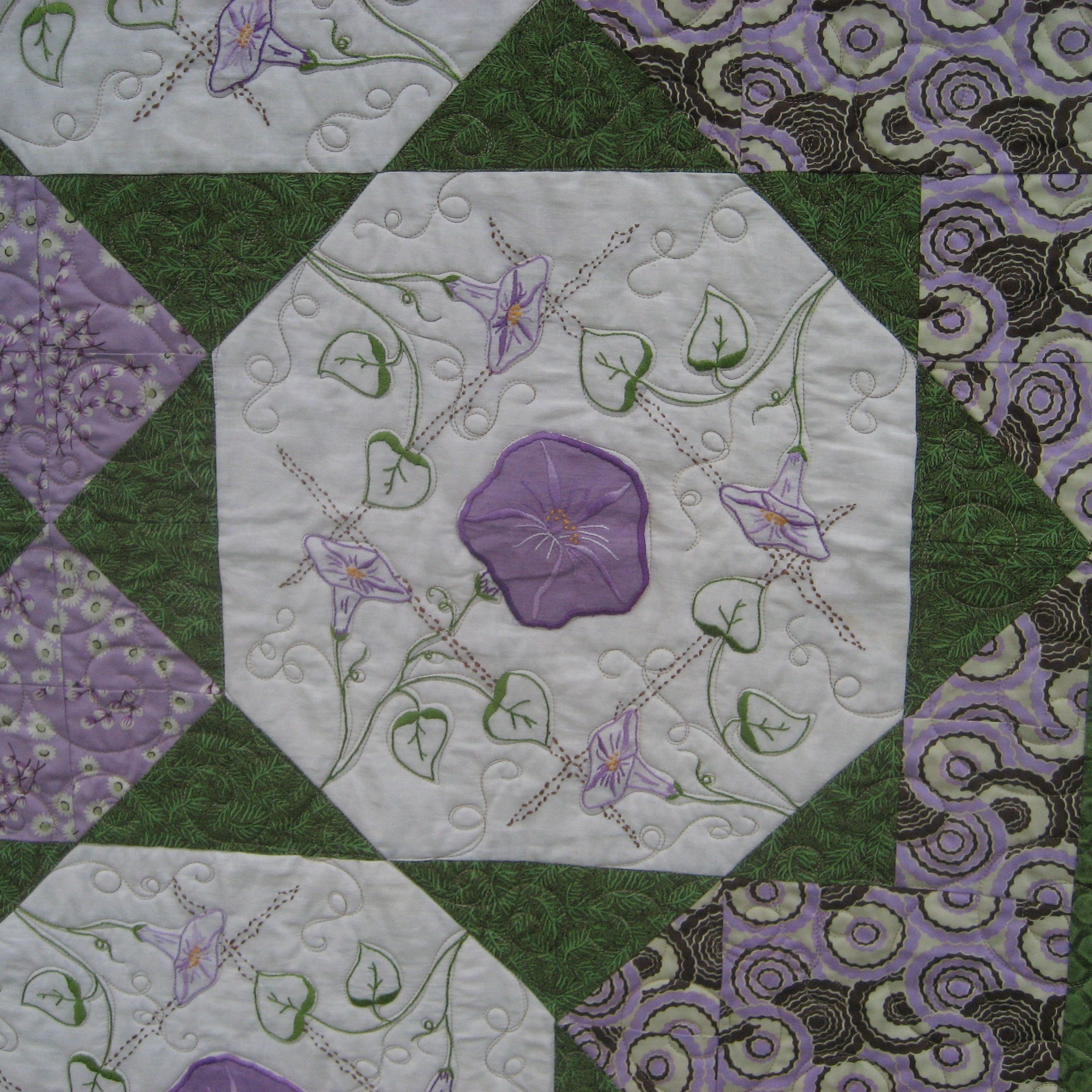 Close up of a quilt block with a floral applique in purple and green