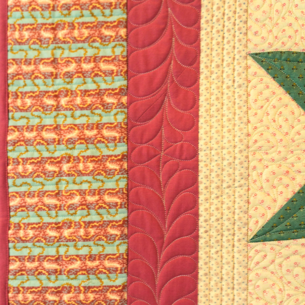 Close-up of a quilted textile with vertical patterned panels in coral, mint, red, cream, and green star shapes.