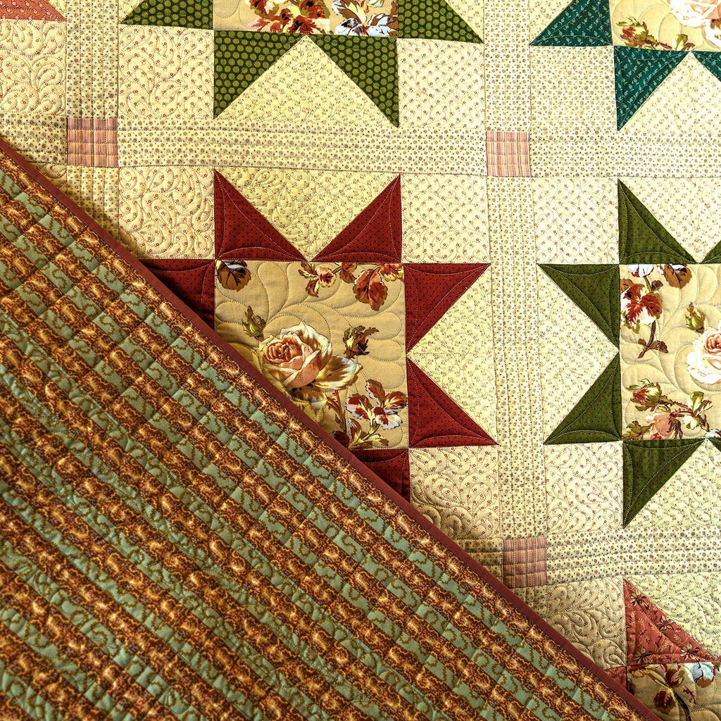 A close-up of a quilted fabric surface showing a diagonal split between a textured striped side in muted green and rust orange, and a patterned side with cream, green, and burgundy starburst blocks.