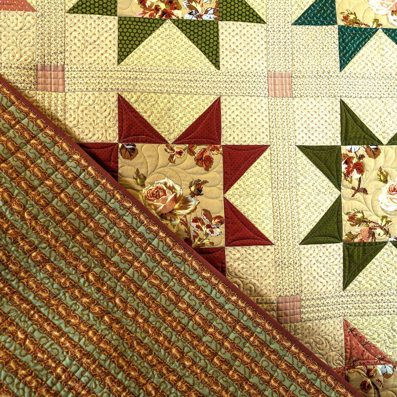 A close-up of a quilted fabric surface showing a diagonal split between a textured striped side in muted green and rust orange, and a patterned side with cream, green, and burgundy starburst blocks.