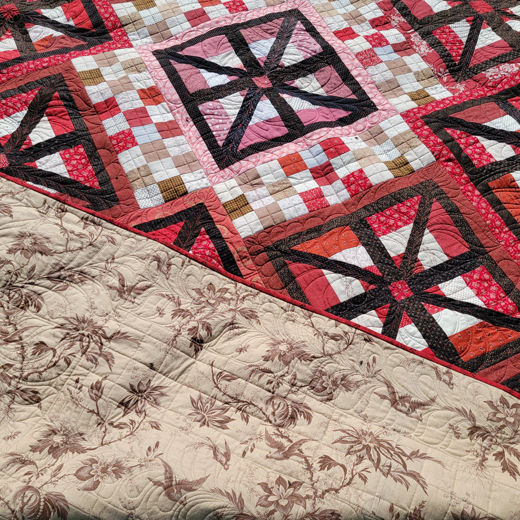 A close up of a quilt in black and red with square prints and the backing showing a neutral floral print. 
