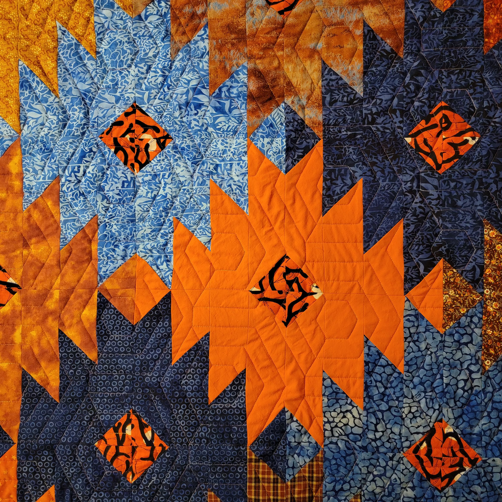 Close up on ikat print quilt in blue and orange in a honeycomb pattern. 