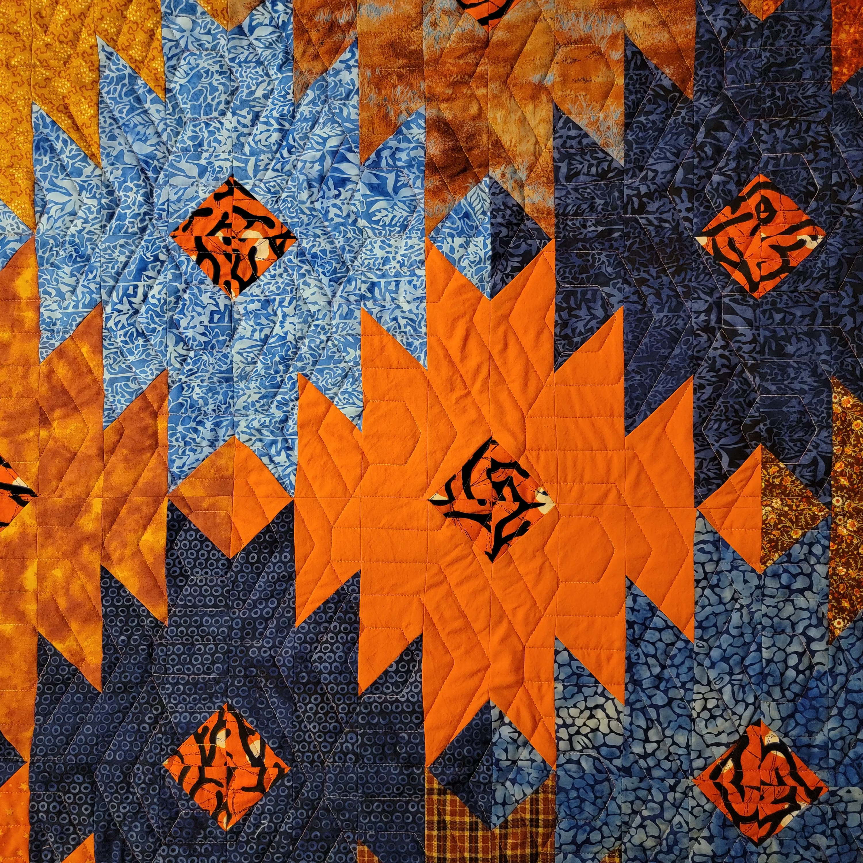 Close up on ikat print quilt in blue and orange in a honeycomb pattern. 