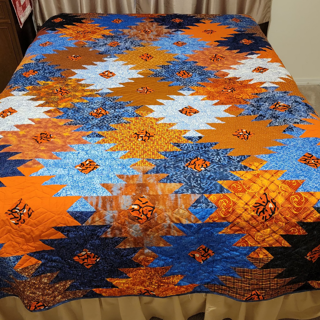 Orange and blue ikat print quilt in a honeycomb print laid out on a bed.