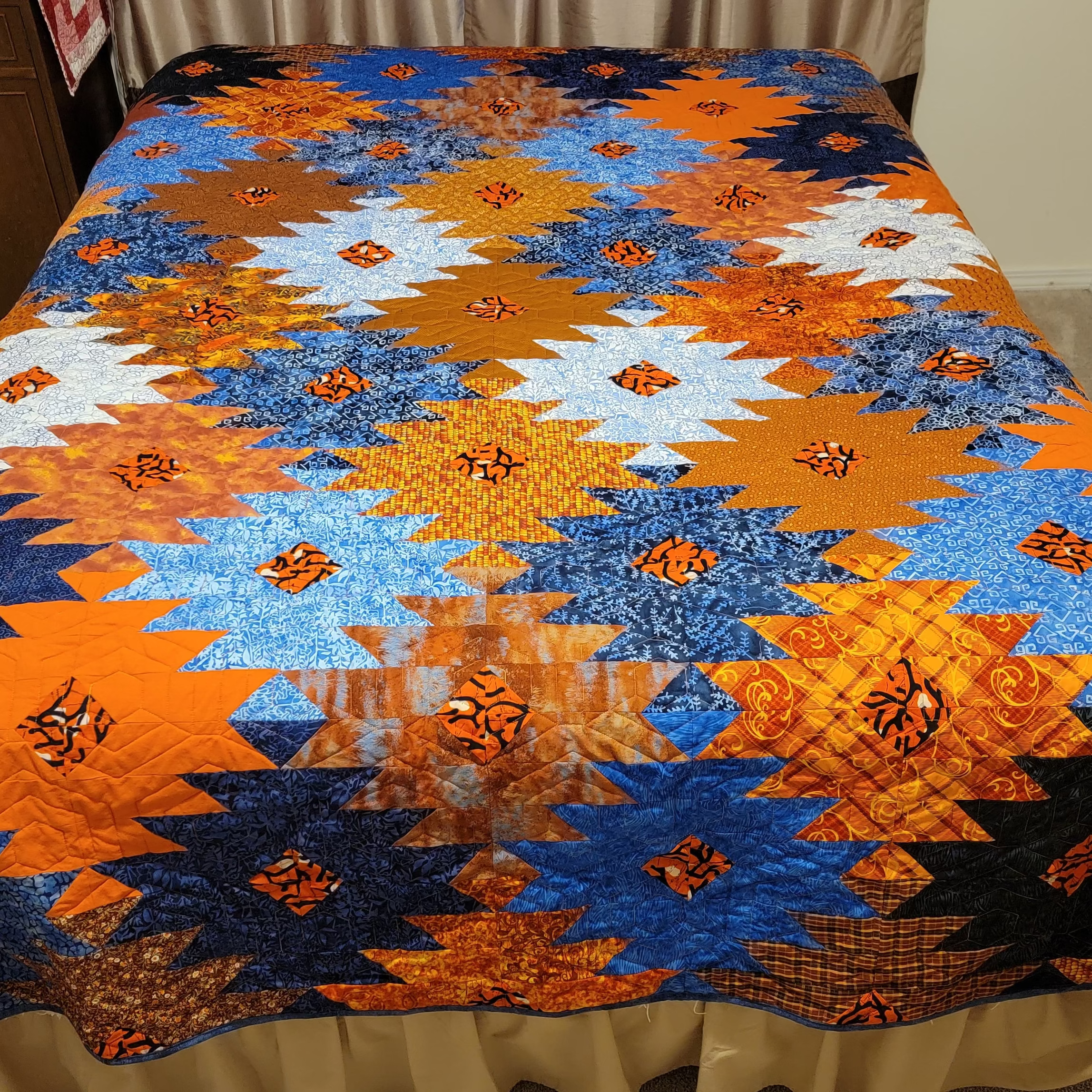Orange and blue ikat print quilt in a honeycomb print laid out on a bed.