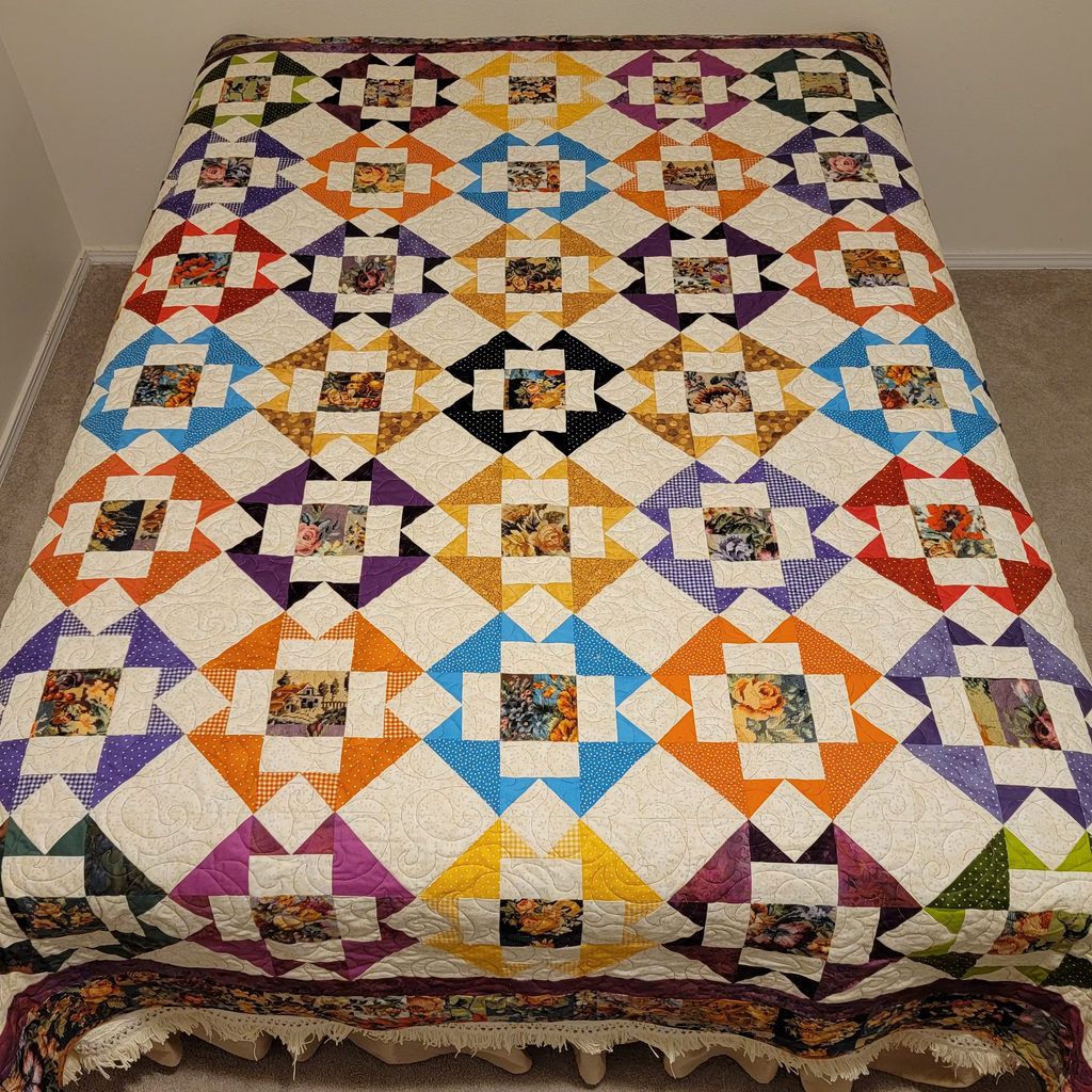 A colorful patchwork quilt with a geometric diamond pattern and floral center squares, spread out on a bed in a simple room with beige walls and carpet.