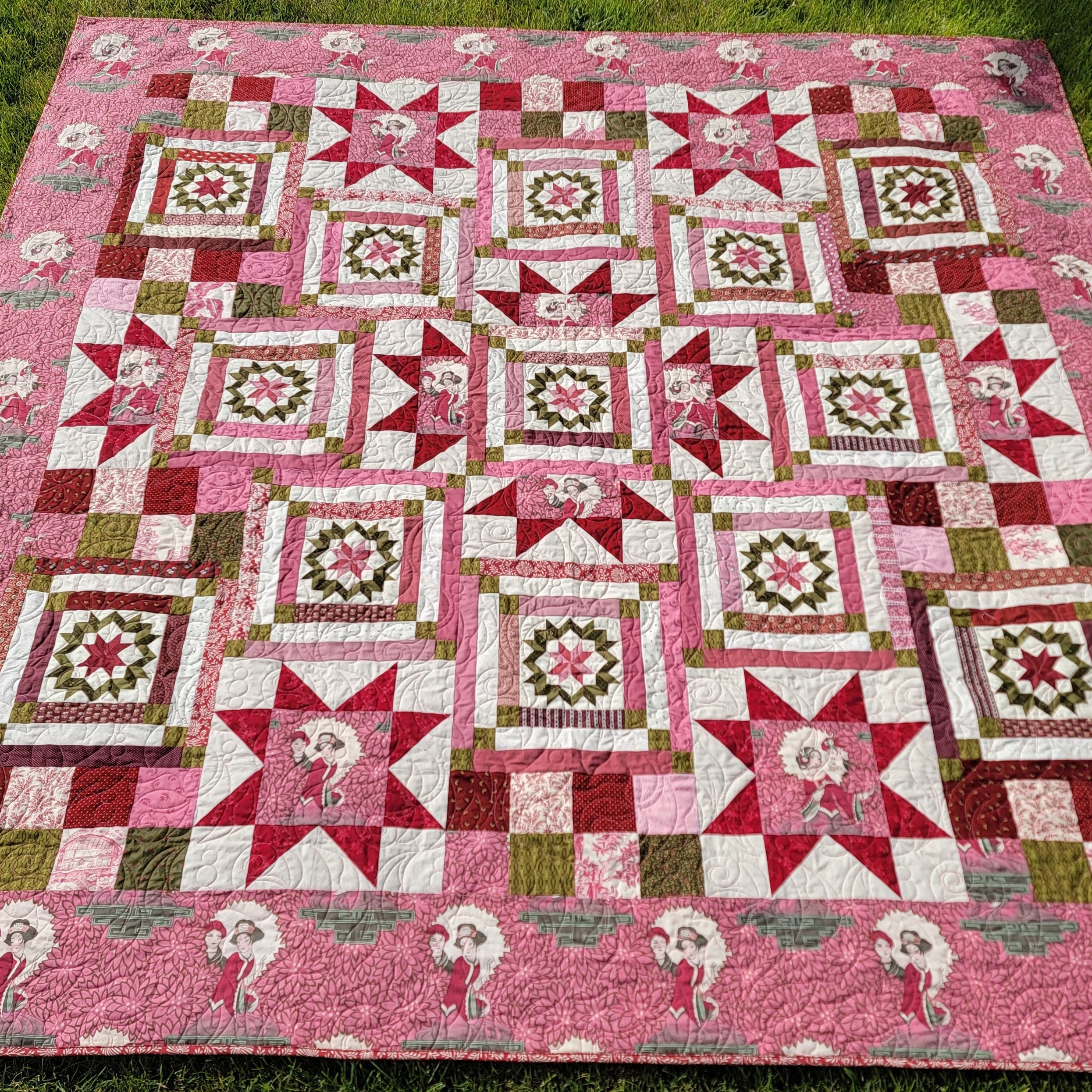Pink geometric and star printed quilt laid out on grass