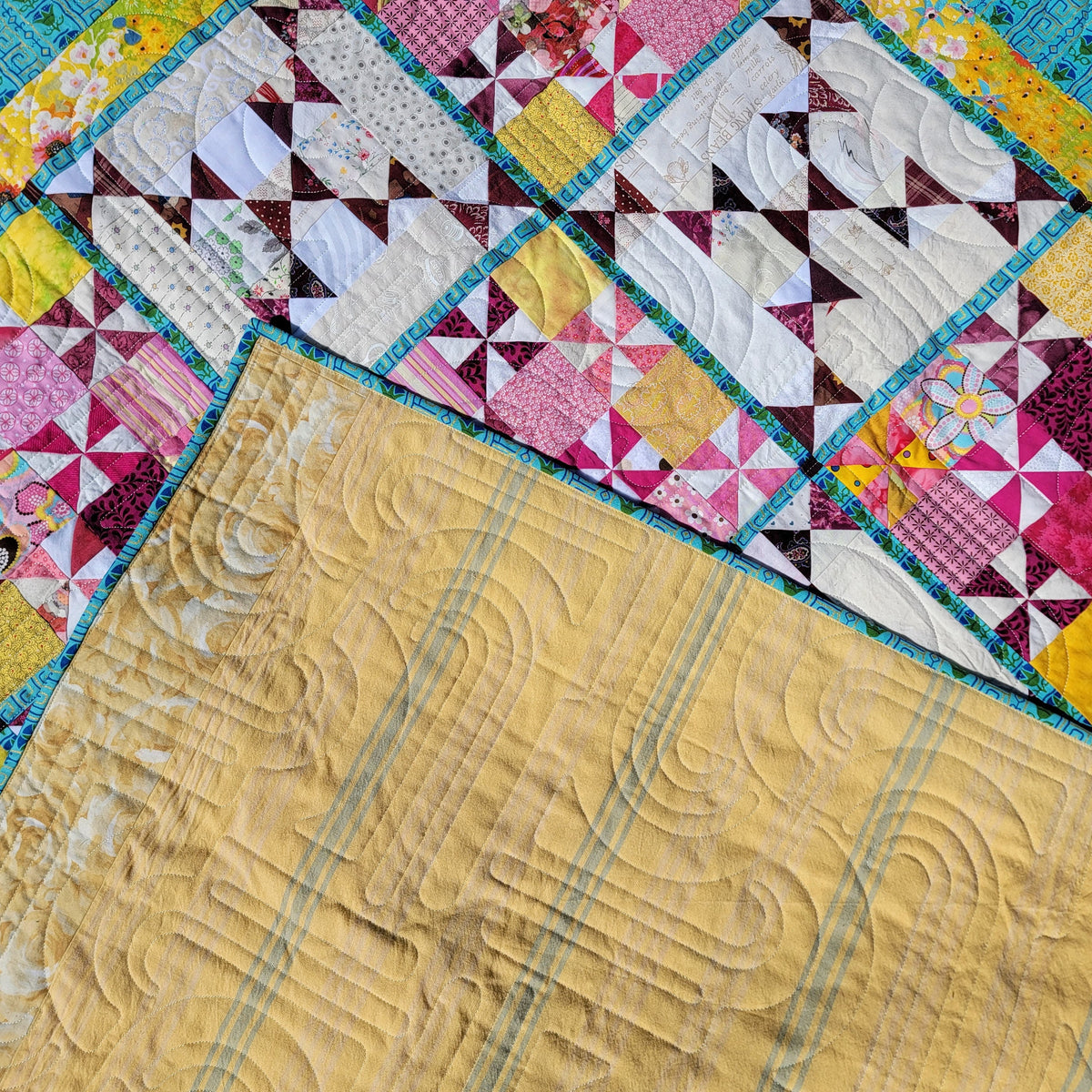 A close-up of a colorful quilted blanket, showing a patchwork design with pink, yellow, white, and teal sections, plus a large yellow quilted section folded over.
