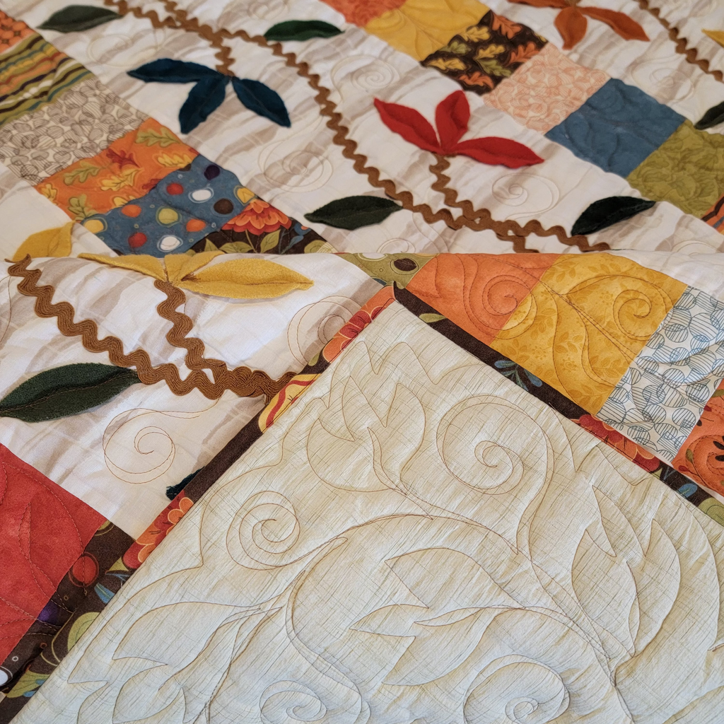 Close-up of a quilted textile product showing a cream-colored quilted section in the foreground with swirling stitched patterns, and a multicolor patchwork section in the background with floral and geometric fabric squares.