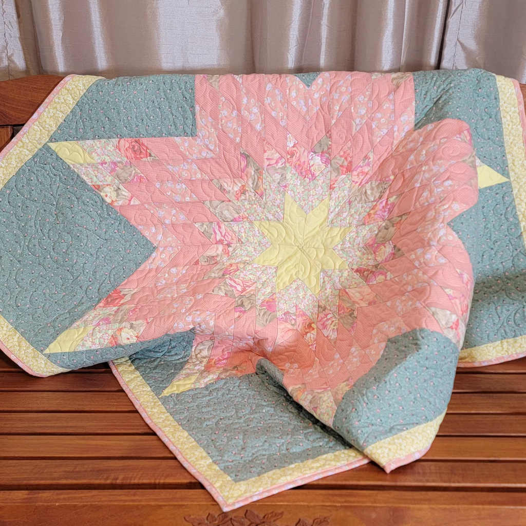Quilt displayed on a wooden bench. he quilt features a lone star in the centre in pink and yellow with a floral border.