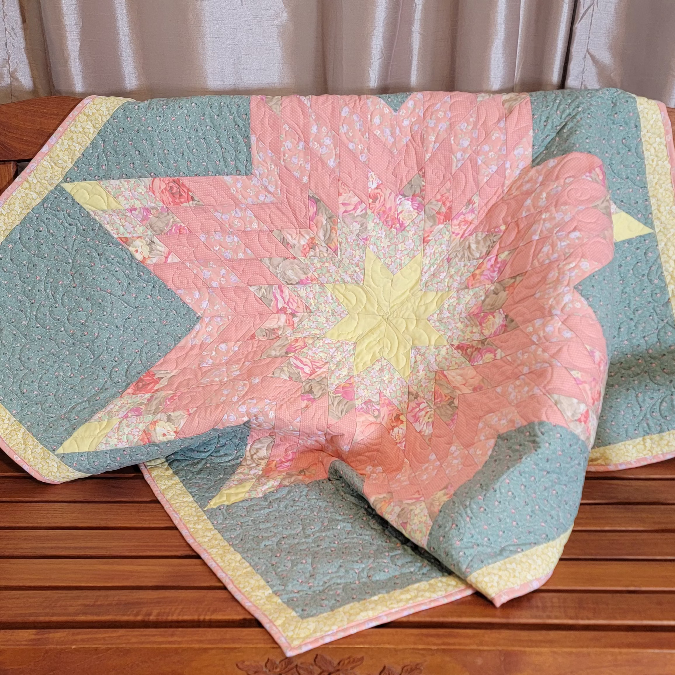 Quilt displayed on a wooden bench. he quilt features a lone star in the centre in pink and yellow with a floral border.