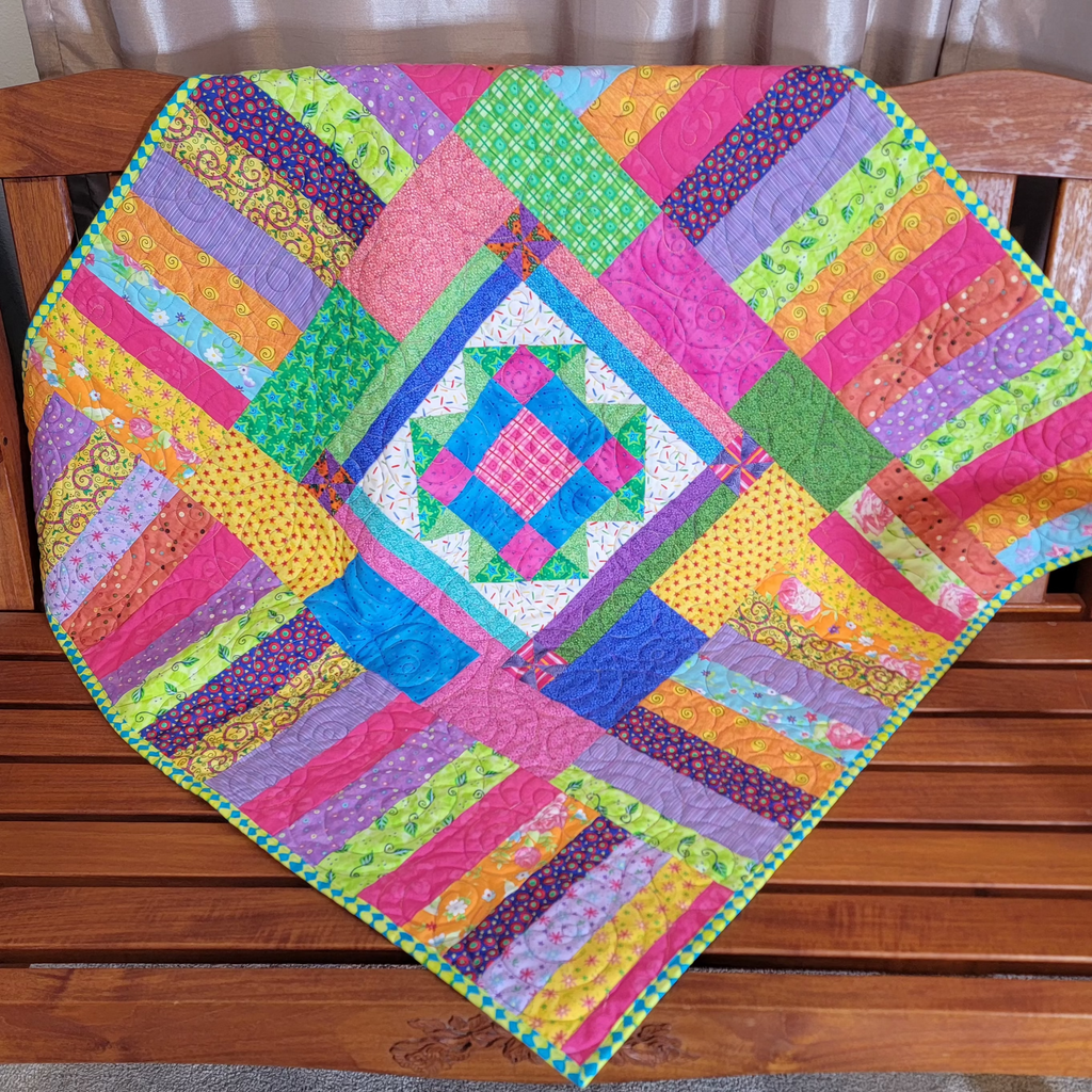 A colorful patchwork quilted blanket with a geometric diamond pattern is draped over a wooden slat bench in an indoor setting.