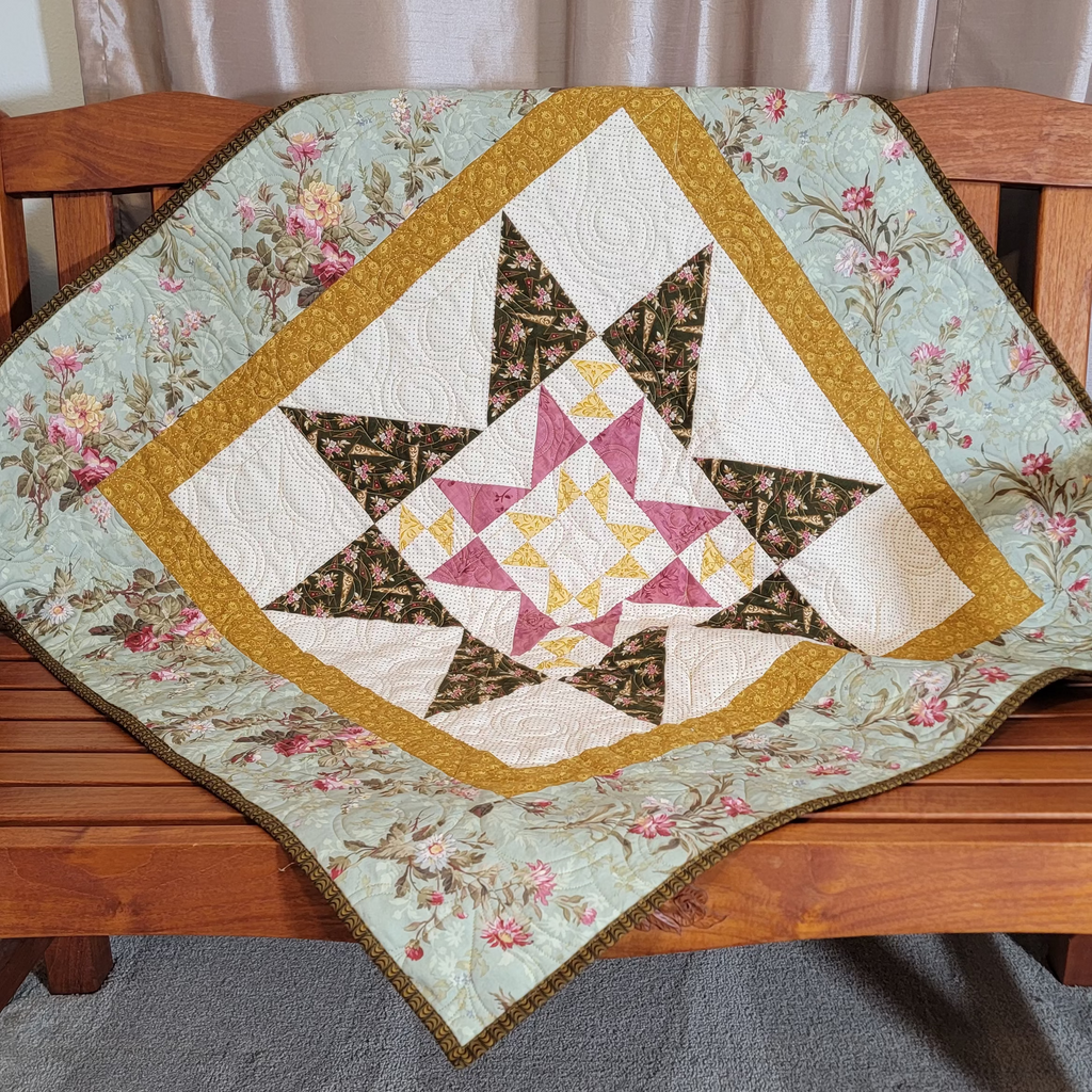 A handmade quilted star-patterned blanket draped over a wooden bench in a home setting, featuring a floral border and geometric star design.