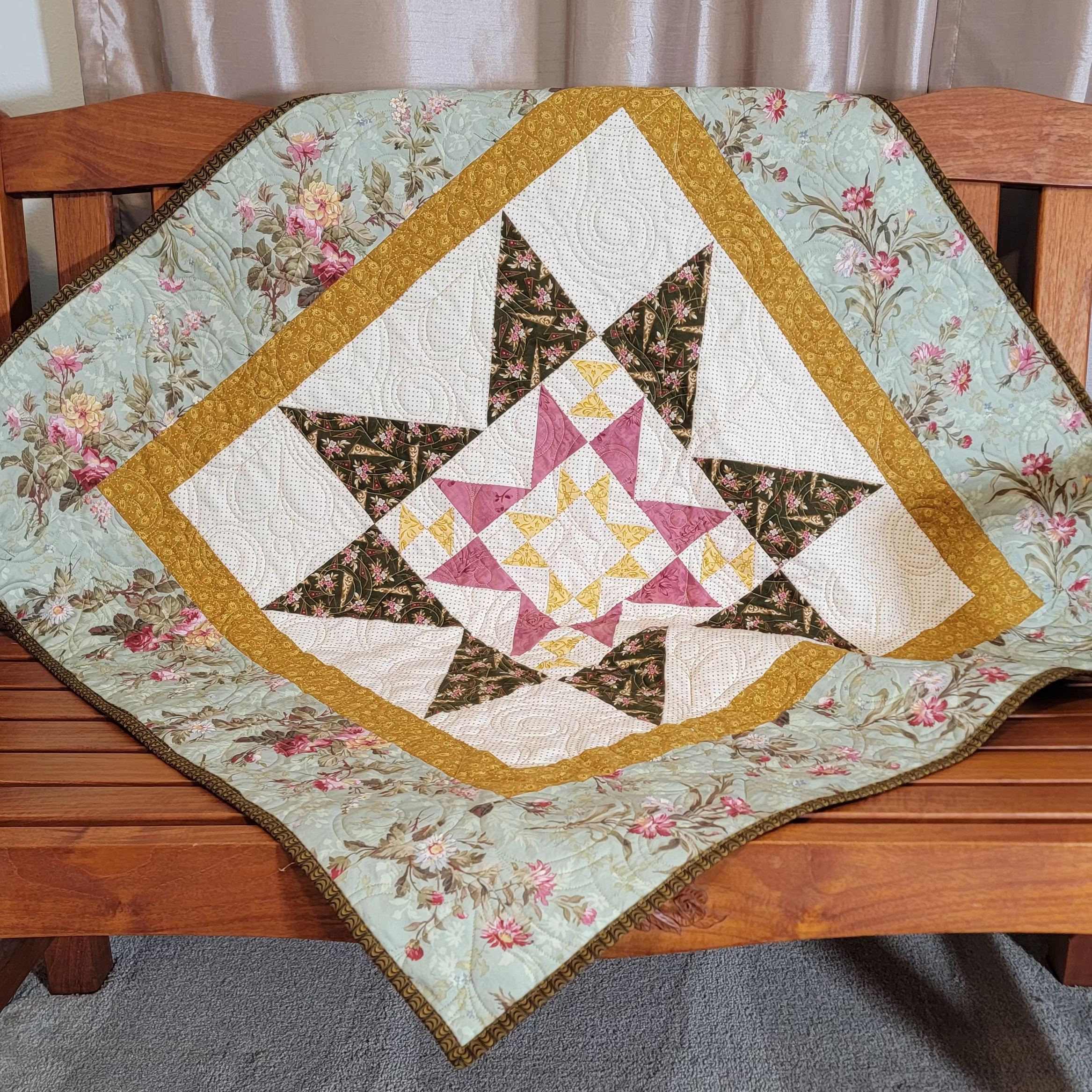 A handmade quilted star-patterned blanket draped over a wooden bench in a home setting, featuring a floral border and geometric star design.