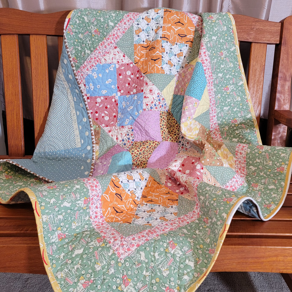 Quilt styled on a wooden bench in pastel green and pink tones with multiple prints and patterns. 