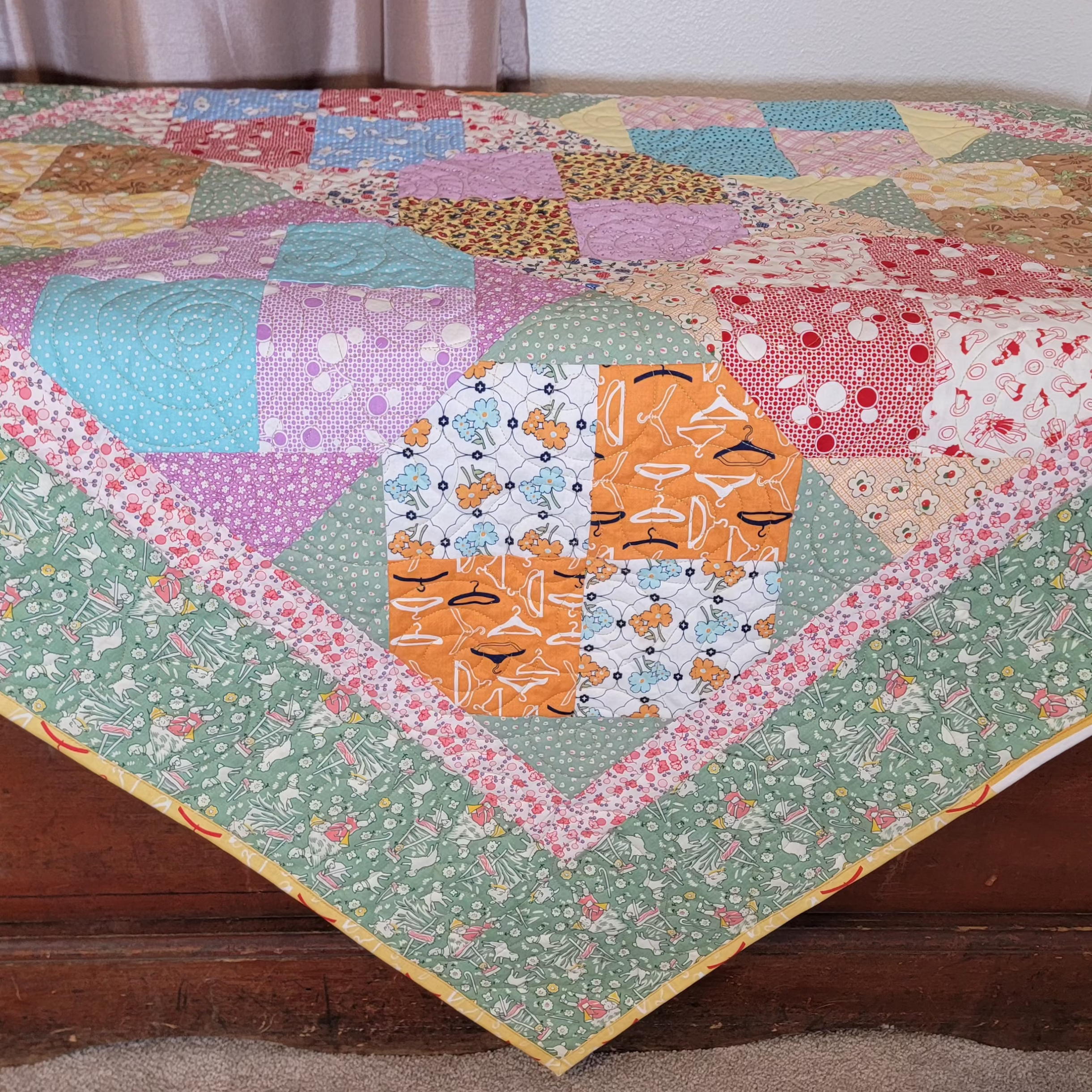Quilt laid out on a wooden chest, the quilt is in pastel green and pink tones in multiple prints and patterns. 
