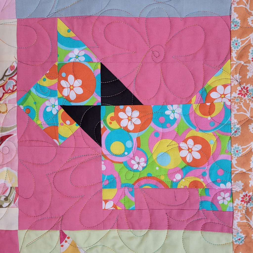 A close-up of a colorful quilted fabric block featuring a stylized dog shape made from pink, floral, and retro circular patterns, with visible quilting stitches.