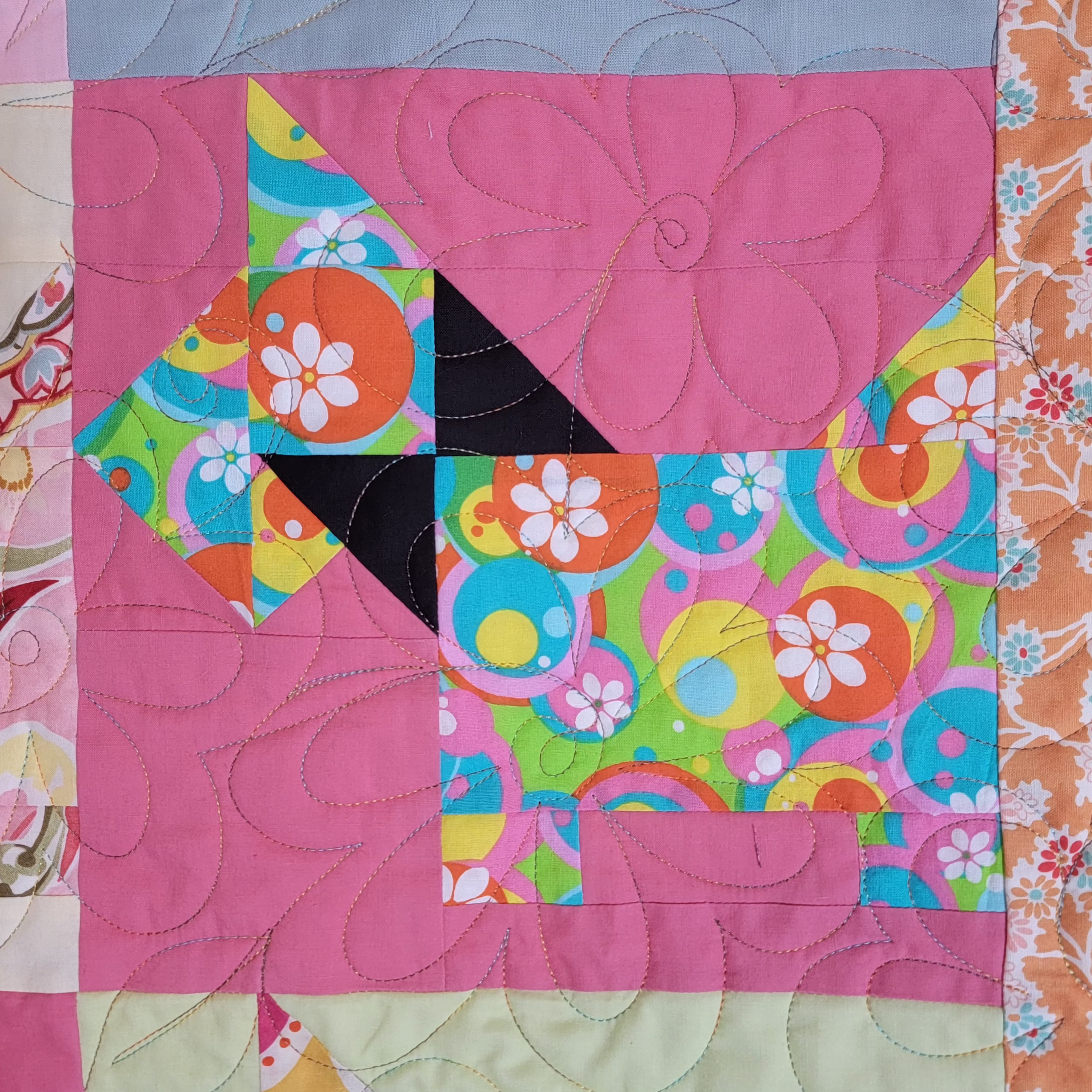 A close-up of a colorful quilted fabric block featuring a stylized dog shape made from pink, floral, and retro circular patterns, with visible quilting stitches.