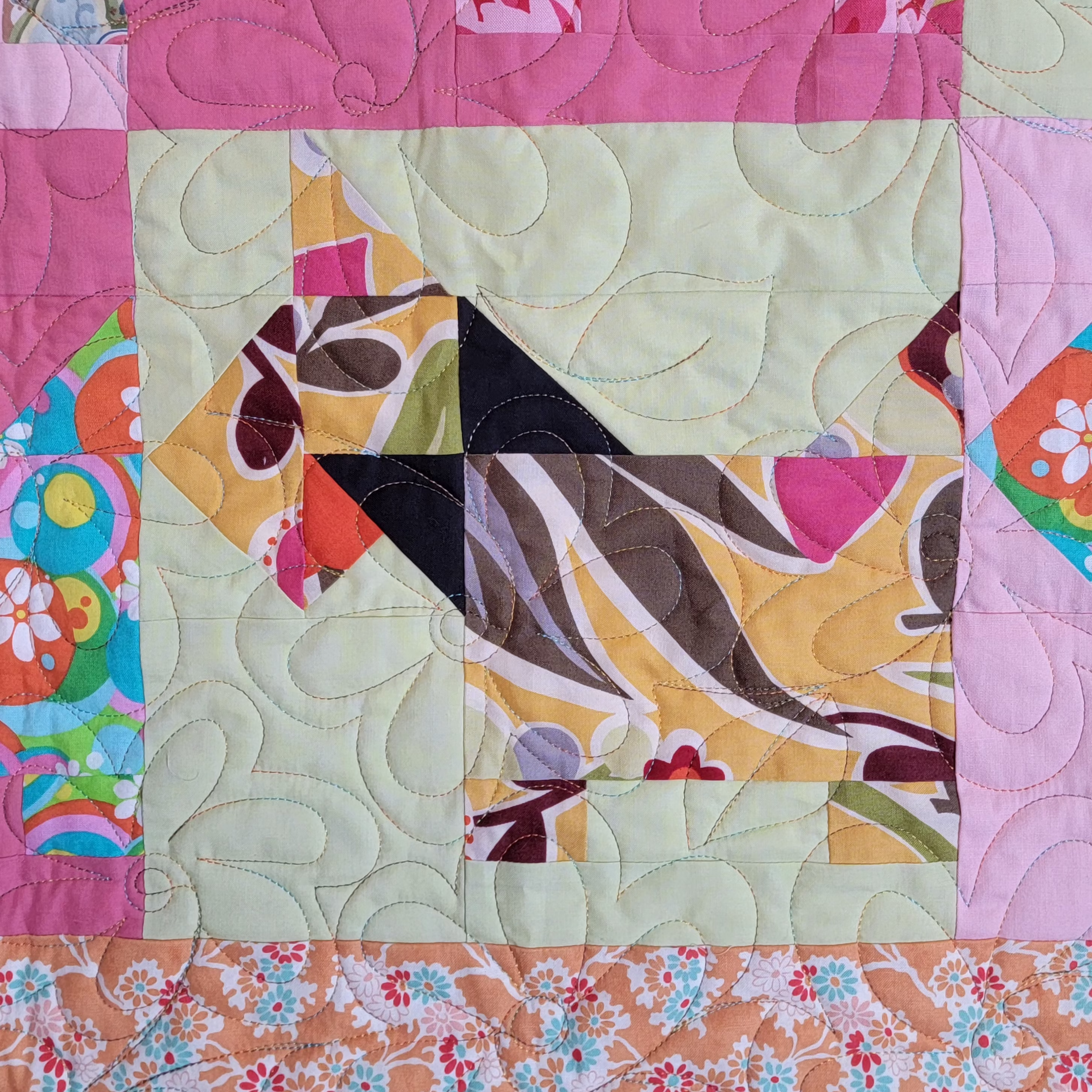 A close-up of a colorful quilted fabric panel featuring a stylized dog patchwork design in yellow, pink, black, brown, and green, surrounded by a light green quilted center and patterned borders.