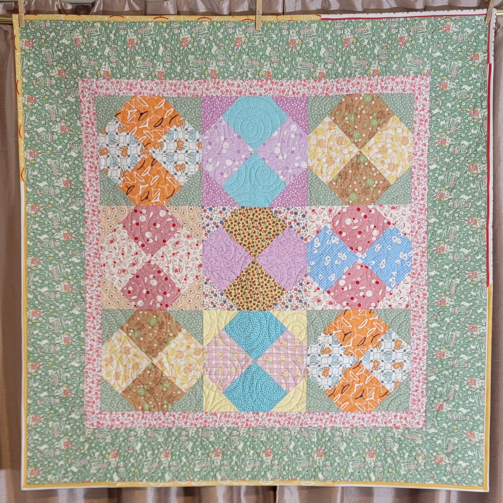 Quilt hung up on a rod, the quilt is made up of pastel green, pink and blue tones in multiple prints and patterns. 