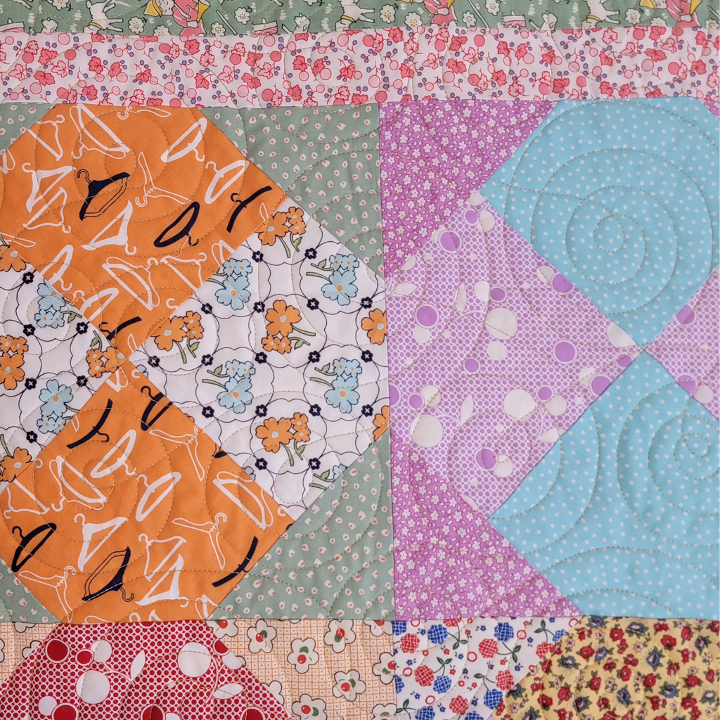 A close up of a handmade quilt made up of diamond prints in the centre in pastel orange, blue and pink prints, bordered with a pink and green print. 