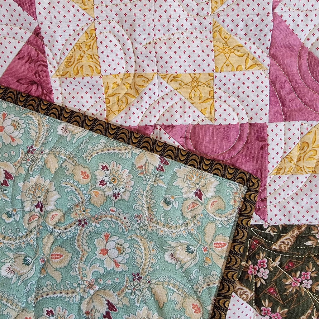 A close-up of a patchwork quilt featuring a star block design in white, yellow, and pink, with a teal floral section and a dark brown patterned border.