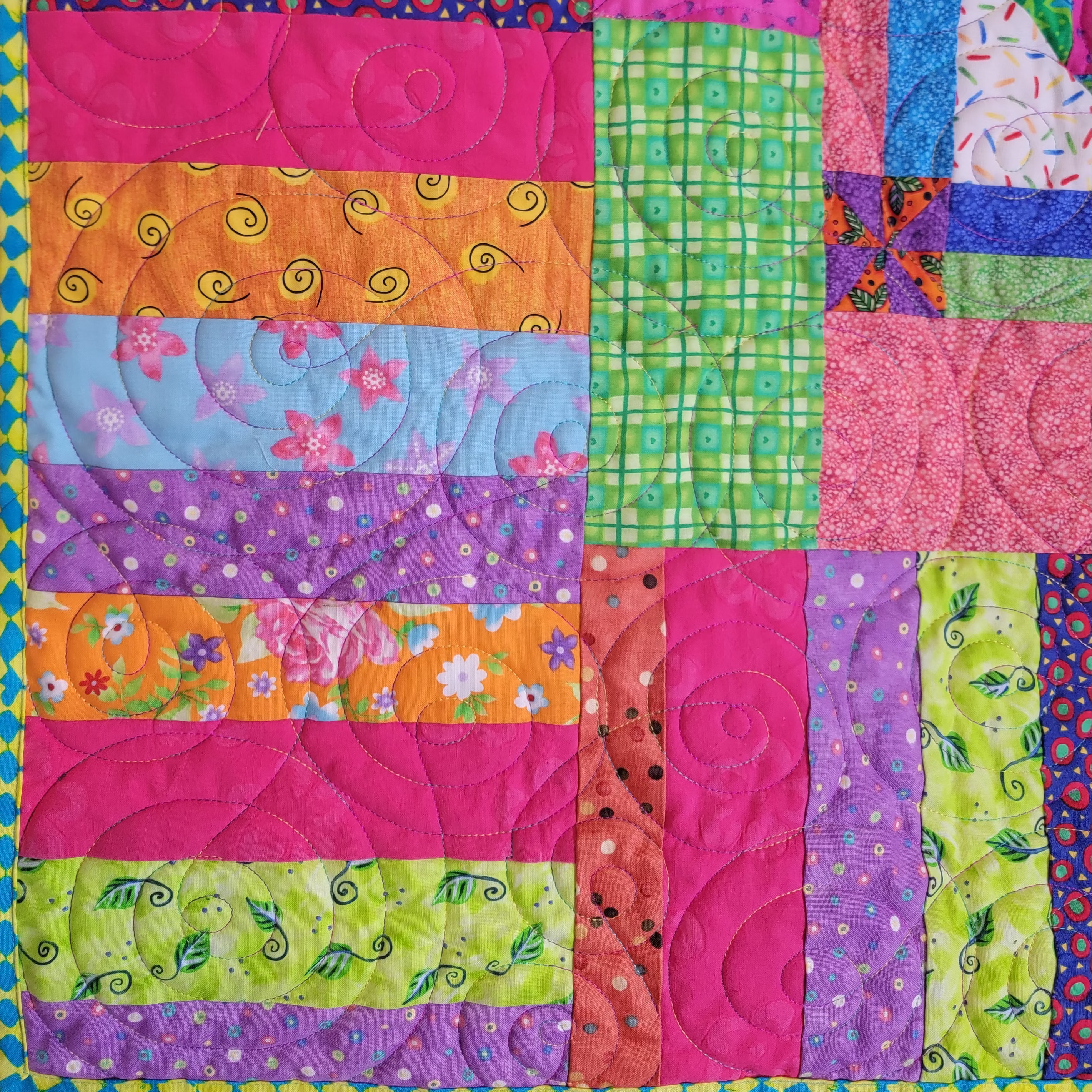 A close up of a handmade quilt in a stripe layout of rainbow colours in multiple prints.  