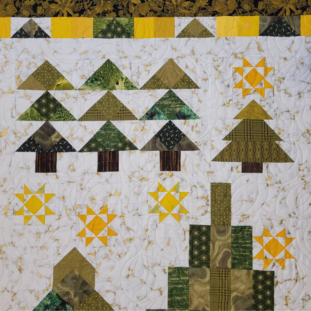 A handmade quilted patchwork blanket featuring a woodland tree and star pattern in shades of green, yellow, and brown on a white background, finished with a floral green and yellow border.