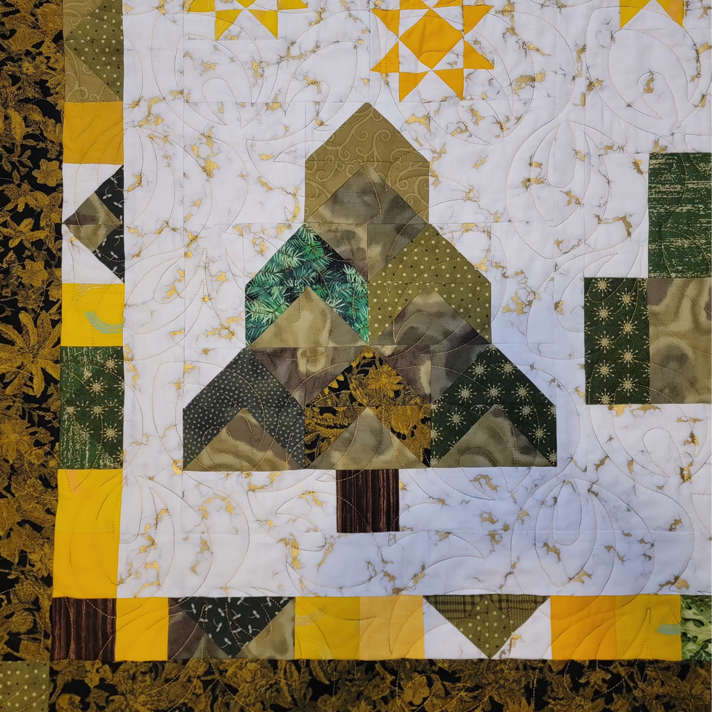 A close-up of a quilted fabric panel featuring a tree design in green, yellow, and brown tones, bordered by a floral patterned edge.
