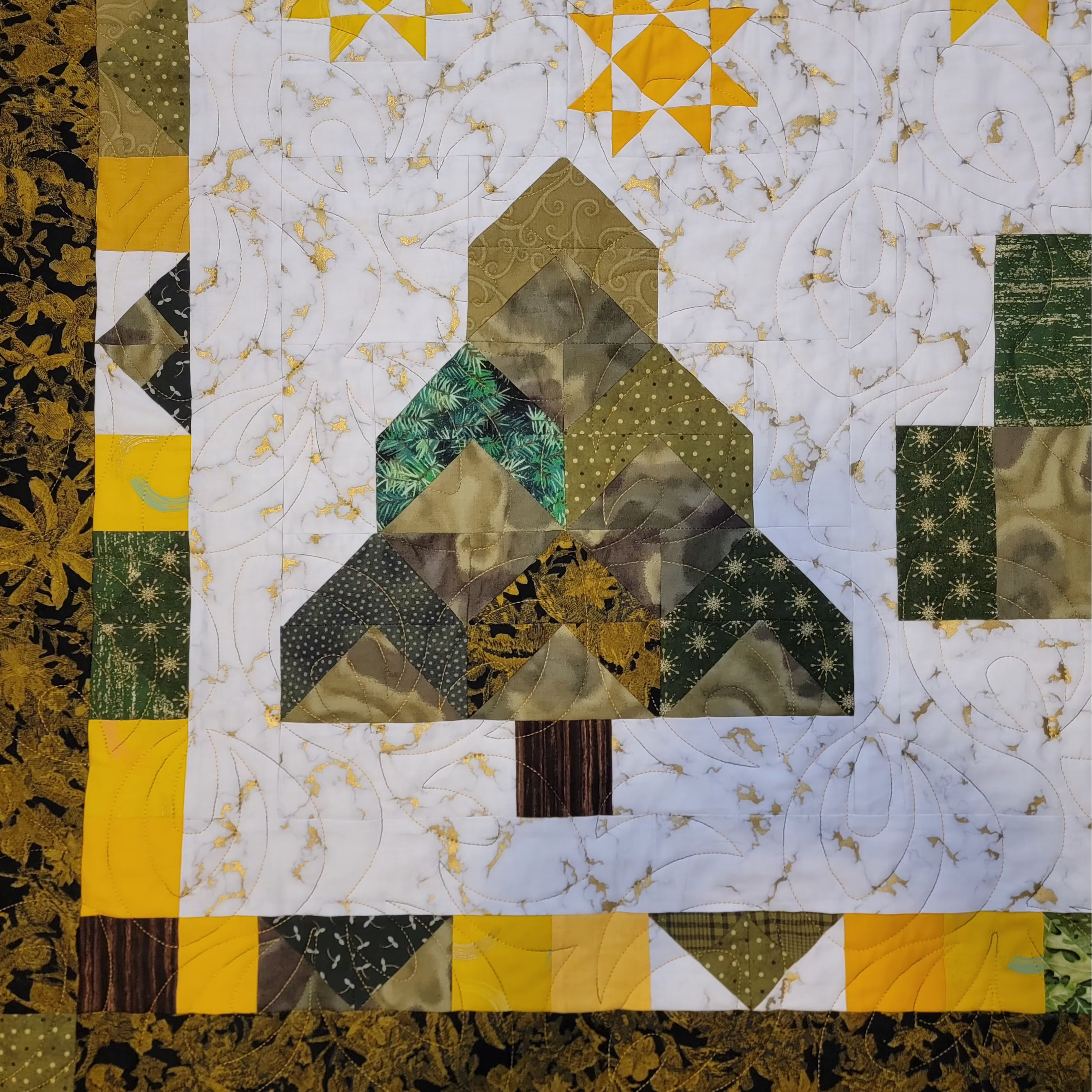 A close-up of a quilted fabric panel featuring a tree design in green, yellow, and brown tones, bordered by a floral patterned edge.