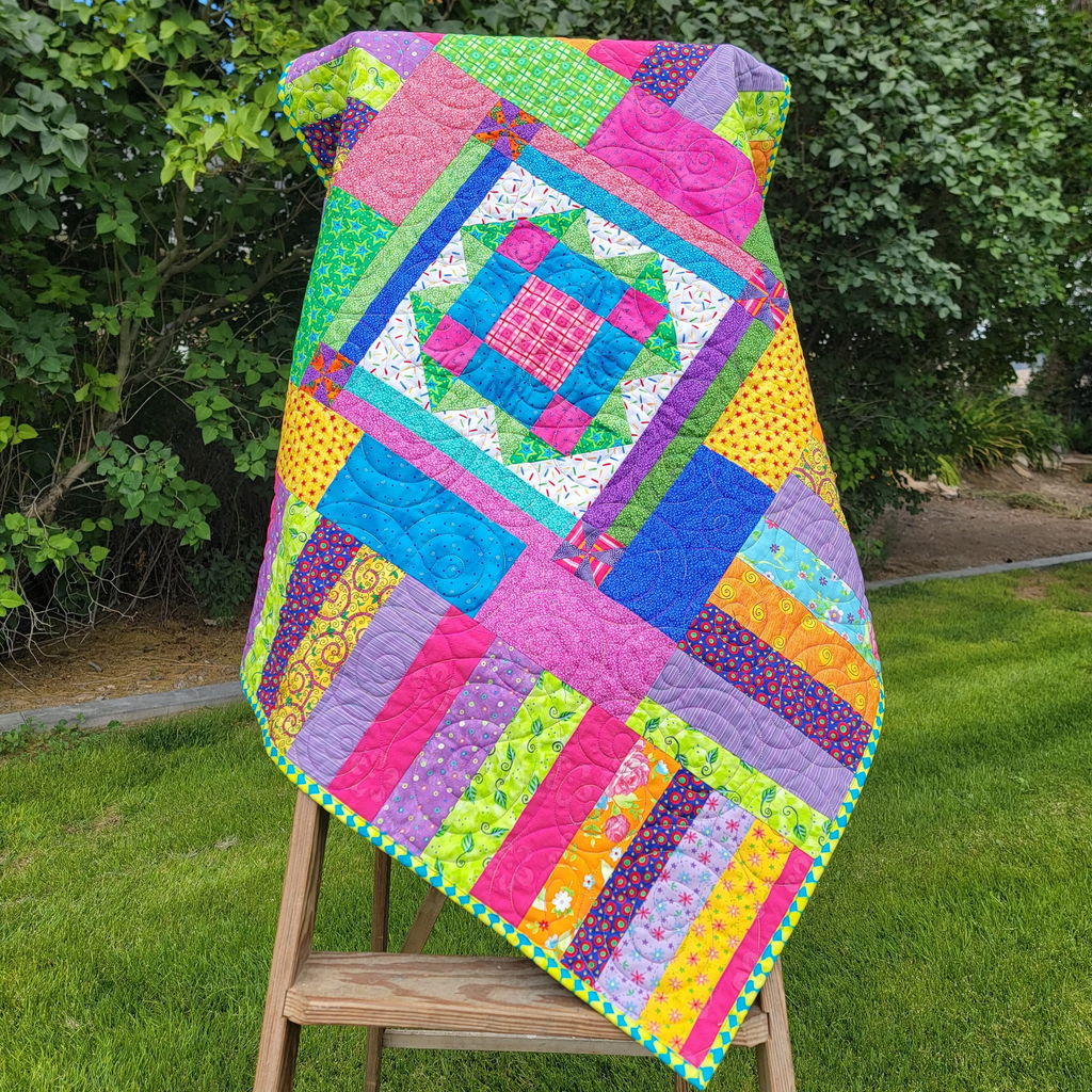 A colorful patchwork quilted blanket with a geometric diamond pattern is draped over a wooden easel in an outdoor setting.
