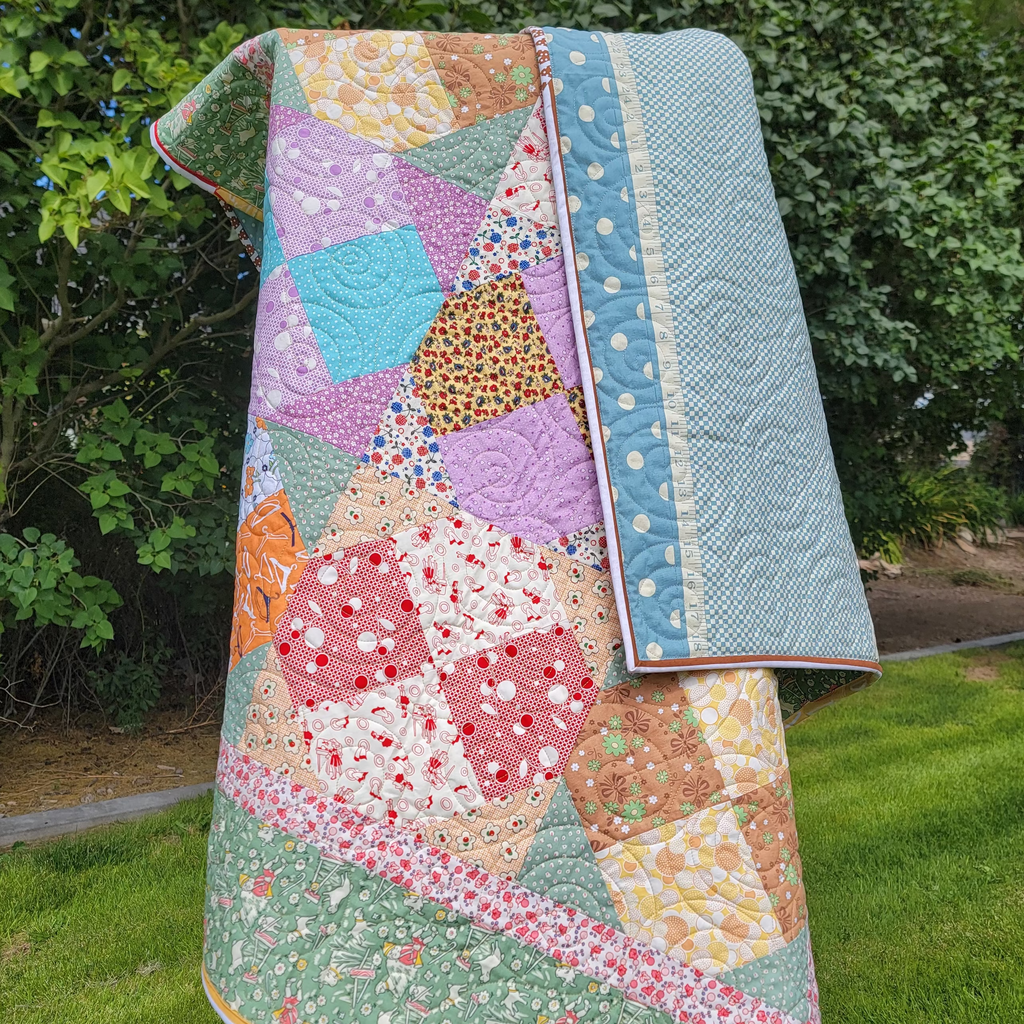 Quilt hung over a wooden easel in pastel green and pink colours in multiple prints and patterns. 