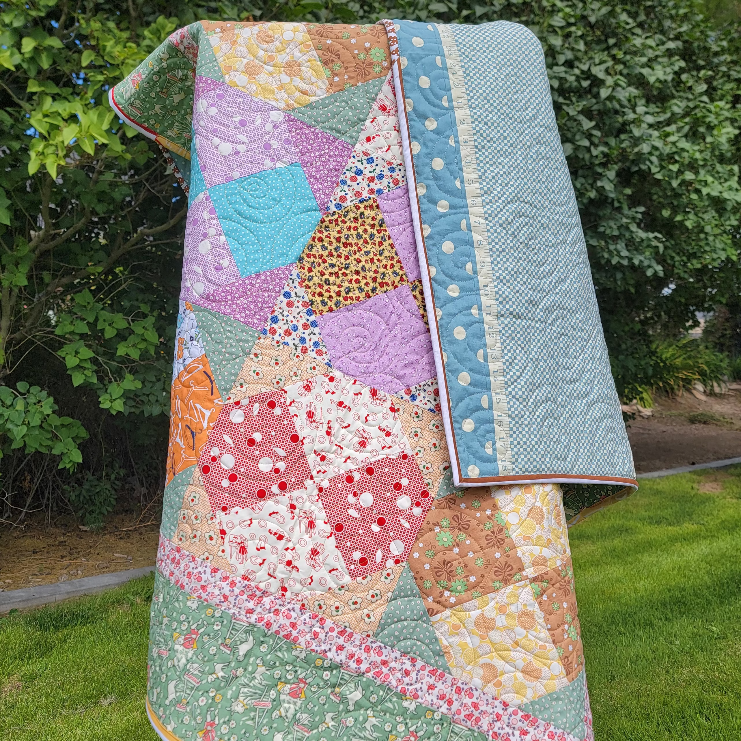 Quilt hung over a wooden easel in pastel green and pink colours in multiple prints and patterns. 