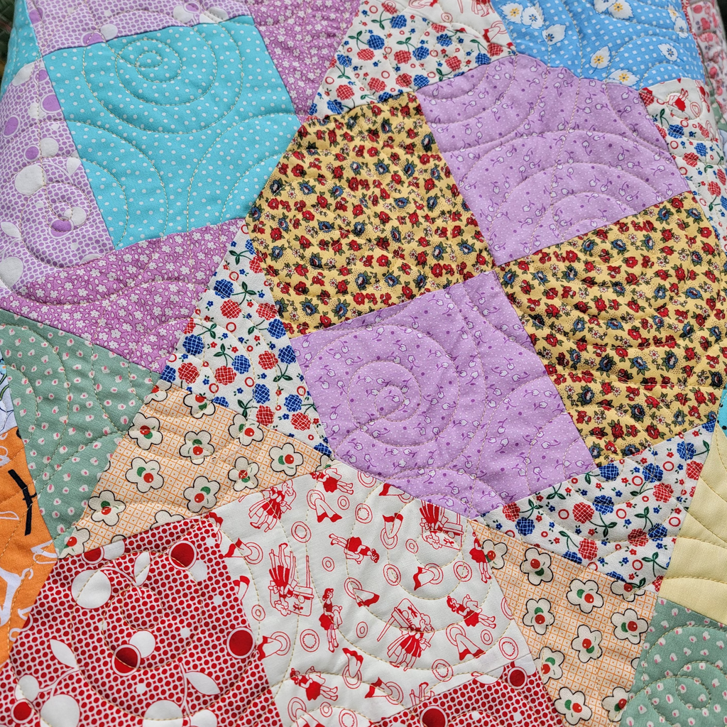 A close up of a handmade quilt made up of multiple prints in pastel colours. 