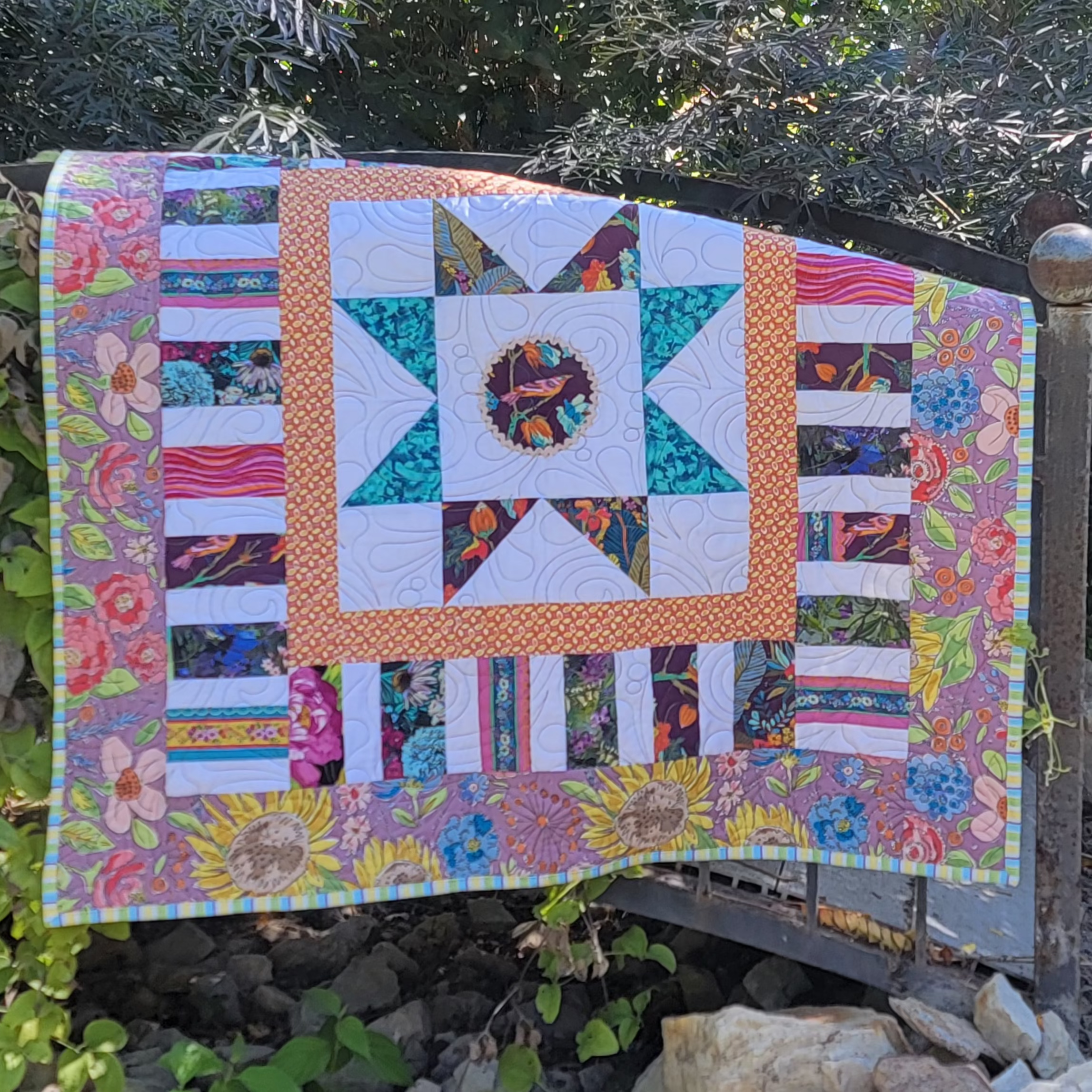 A colorful patchwork quilt draped over a wooden bridge. 