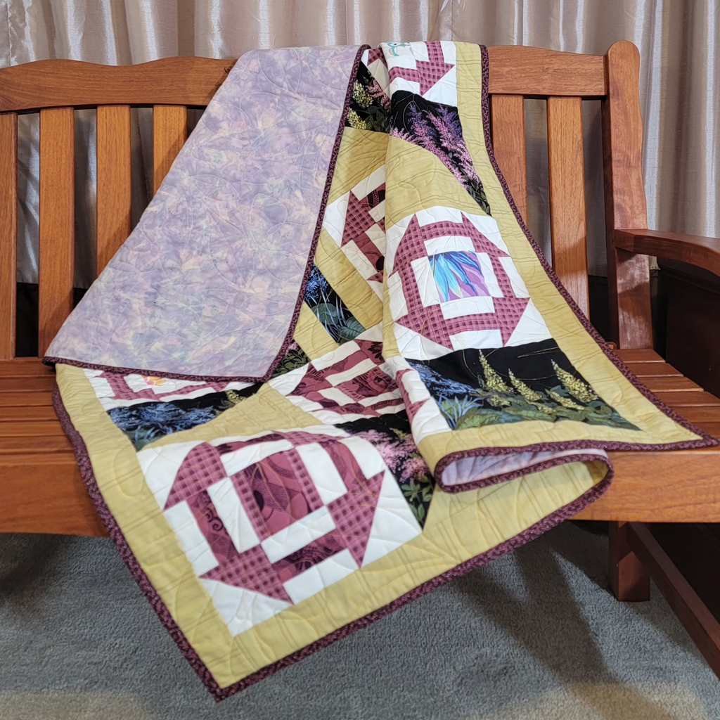 Geometric printed quilt in yellow and pinks with garden inspired prints displayed on a wooden bench. 