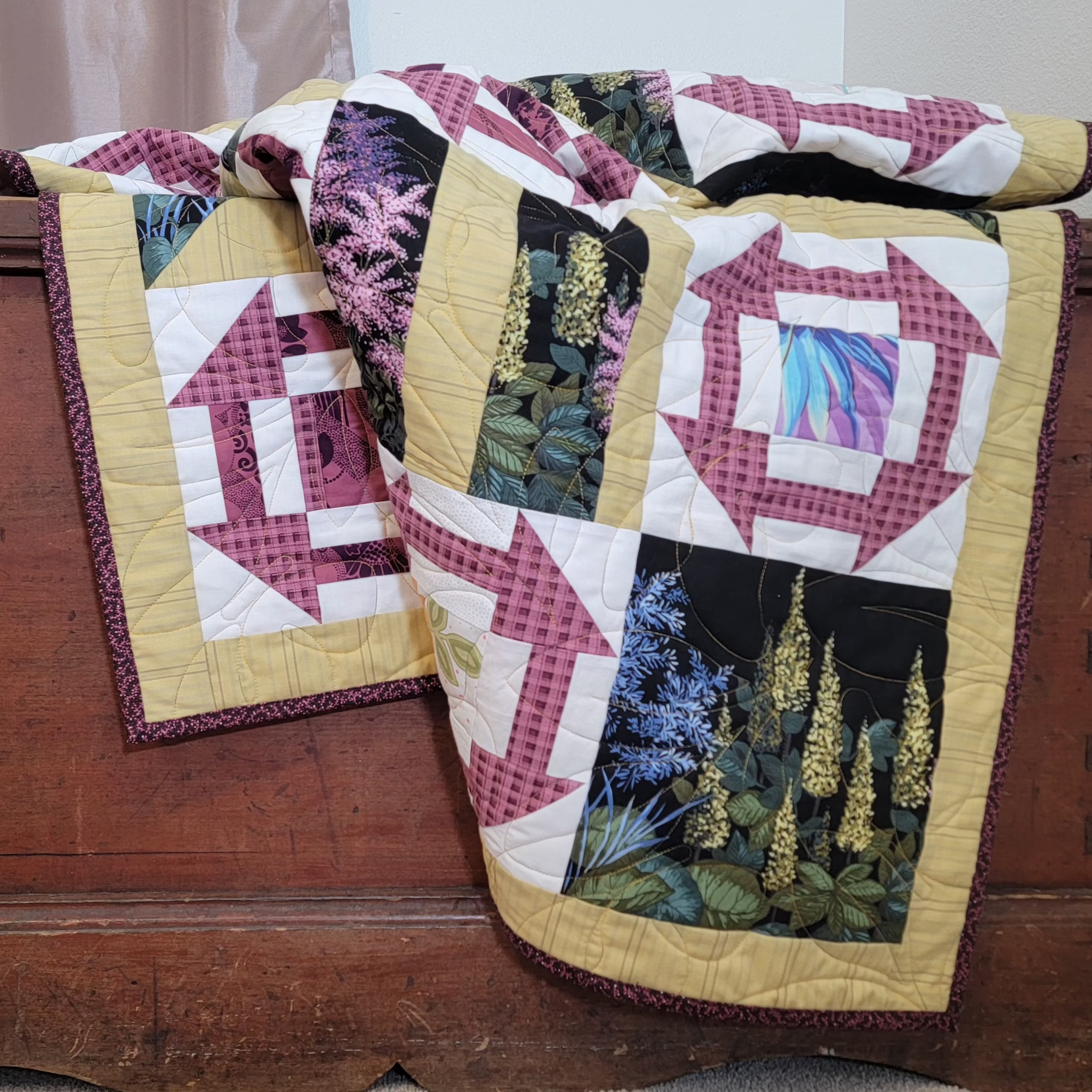 Geometric printed quilt in yellow and pinks with garden inspired prints displayed on a wooden trunk.