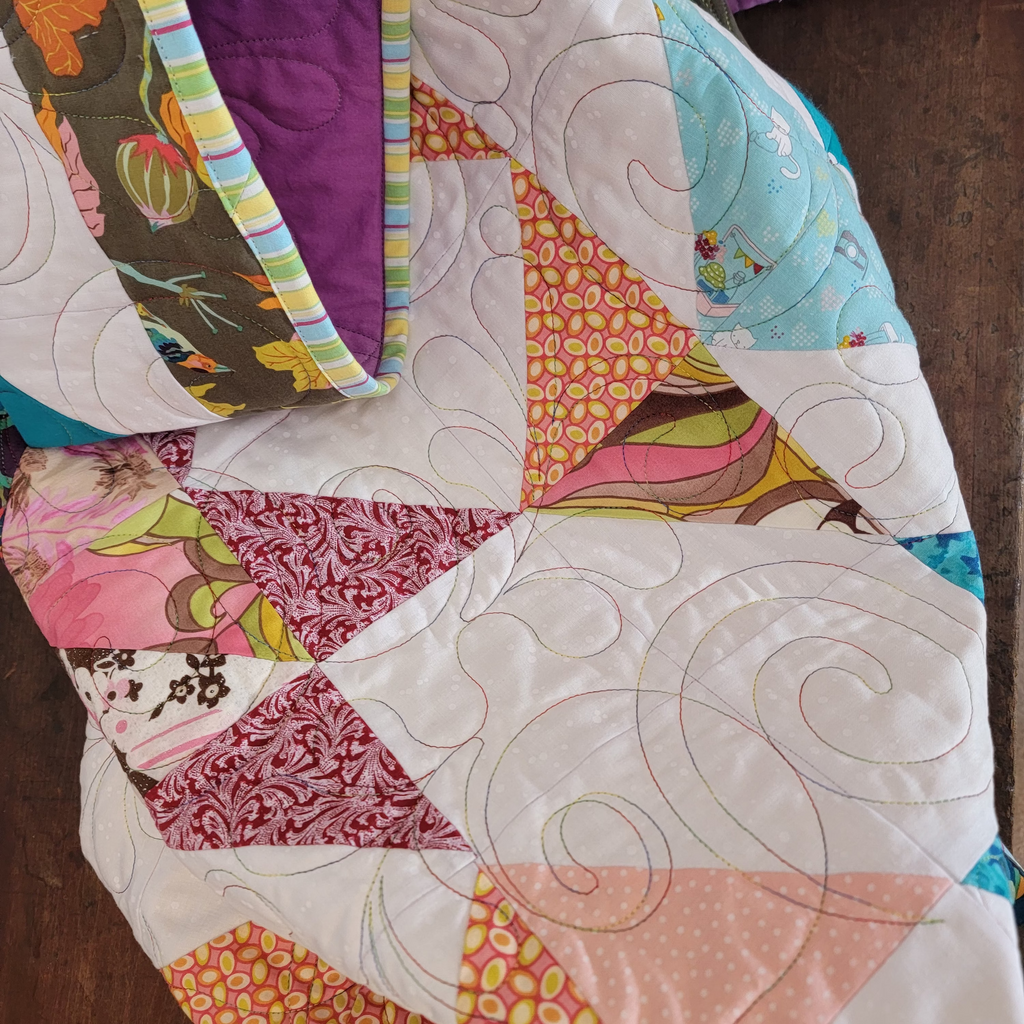 A close up of a quilt with multiple prints with a solid white background with ombre intricate stitching detail. 