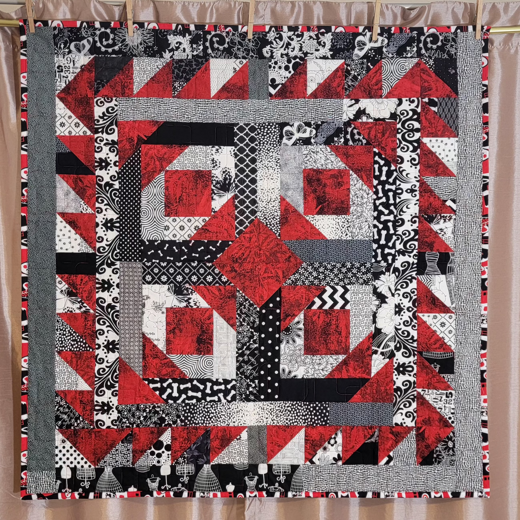 A red, white and black geometric quilt hung up on a golden rail against a dusky pink backdrop.