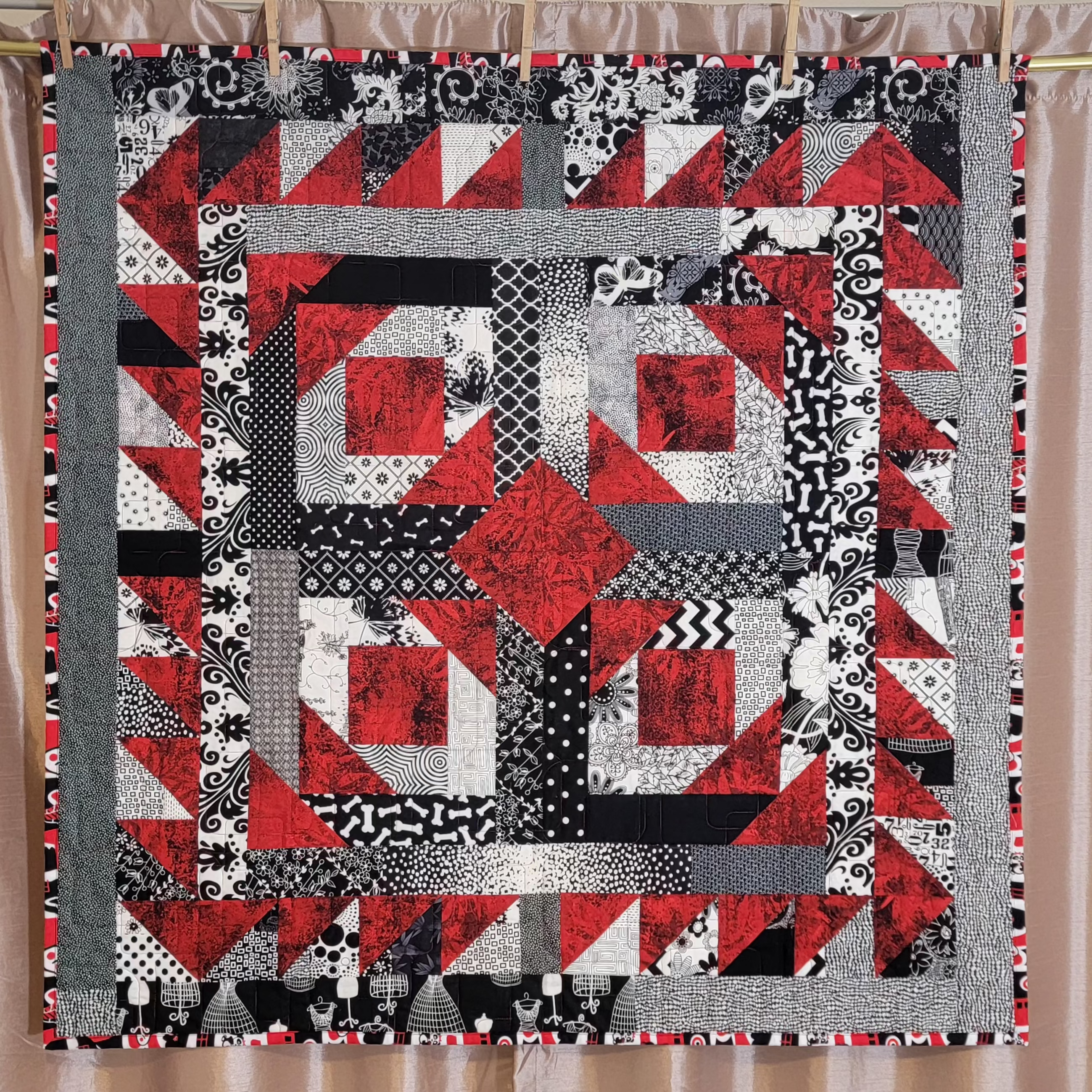 A red, white and black geometric quilt hung up on a golden rail against a dusky pink backdrop.