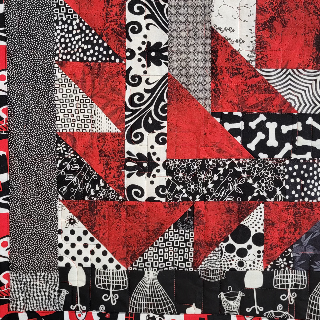A close up of a quilt made up of red, white and black prints with a bold printed border in the same colours. 
