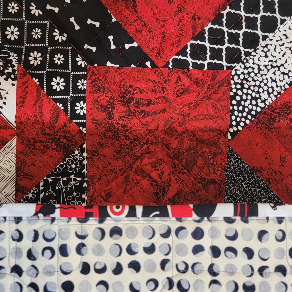 A close up of a quilt in a red, white and black, made up of multiple prints. 