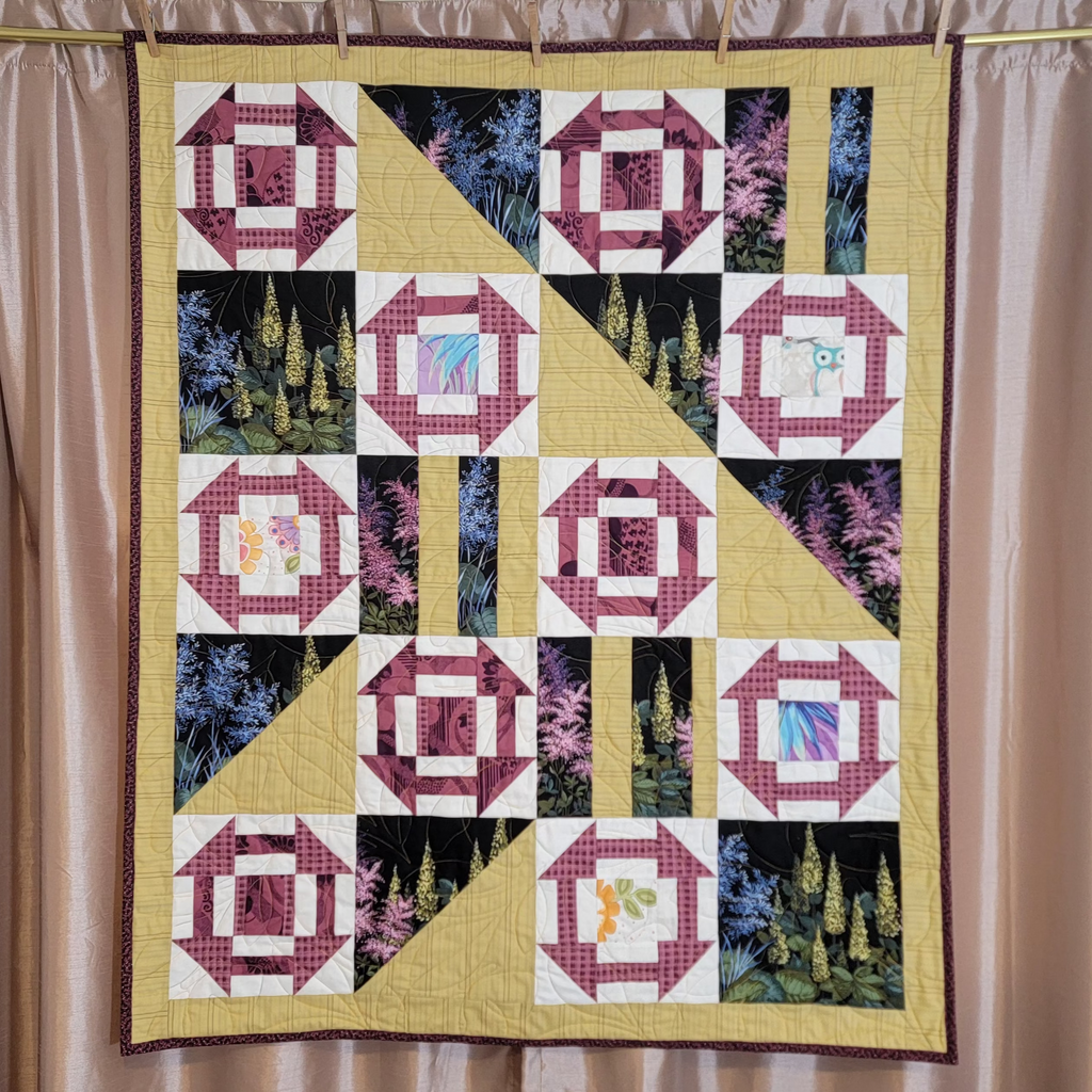 Geometric printed quilt in yellow and pinks with garden inspired prints displayed on a gold bar with a pink satin curtain backdrop.
