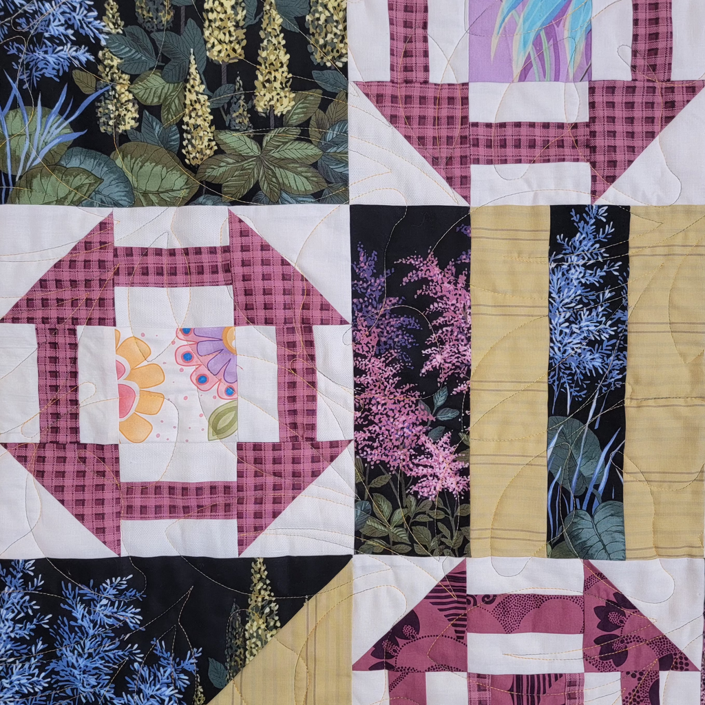 Close up of a quilt with multiple floral and garden inspired prints in 4 different squares made up of triangles and geometric shapes. 