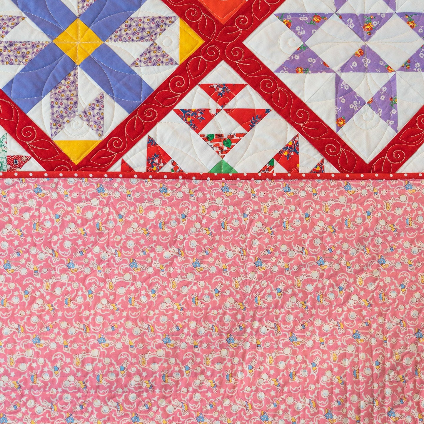 A close-up of a quilted fabric panel with a colorful geometric star pattern across the top and a solid pink floral print across the bottom.