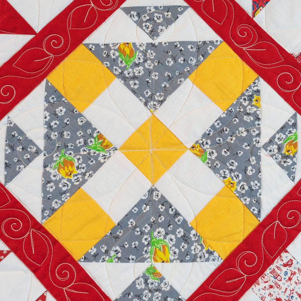 A close-up of a quilted fabric pattern featuring a central geometric star design with yellow and gray floral triangles, bordered by red patterned bands and white sections.
