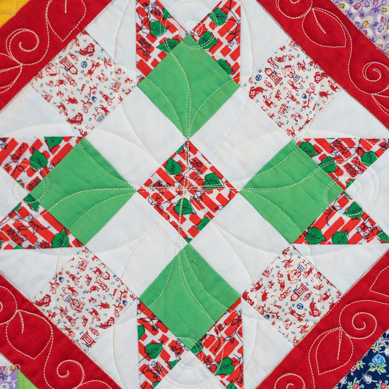A close-up of a quilted patchwork fabric featuring a star design with green, red, and white patterned sections, bordered by red and floral patterned edges.