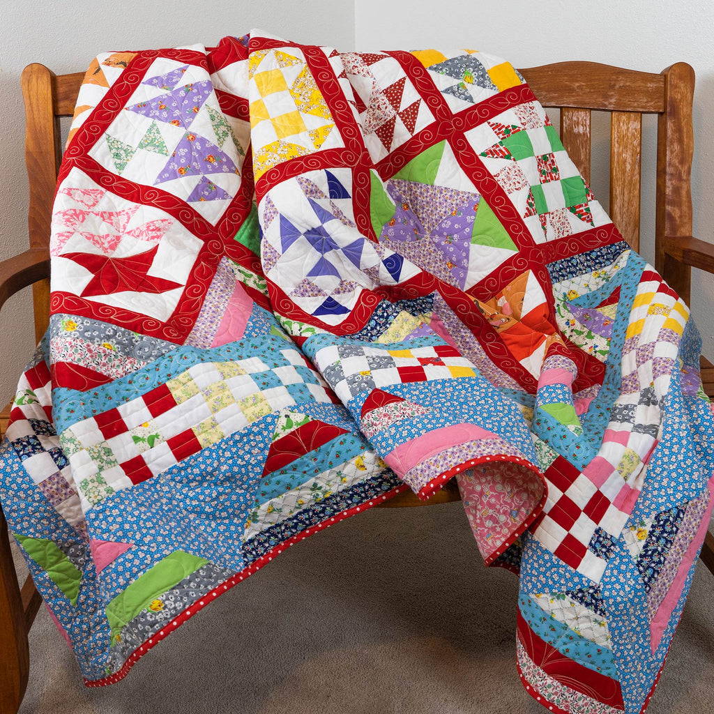 A colorful patchwork quilt draped over a wooden armchair in a home setting, featuring various geometric and floral patterns in red, blue, pink, yellow, green, and white.